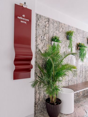 Granite-clad corridor with red Sanskrit signage, hanging planters, and a potted palm