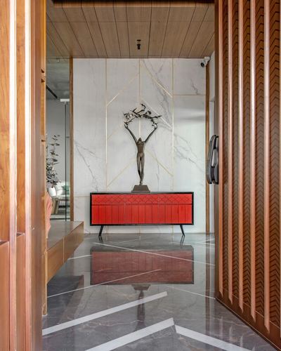 Foyer view through carved wooden door showing marble wall with bronze sculpture above red console