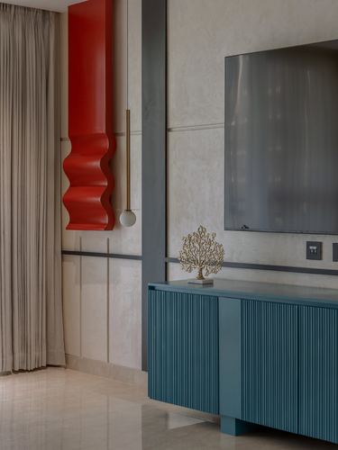 Neutral stone wall with red sculptural panel, pendant light, TV, and teal fluted sideboard below