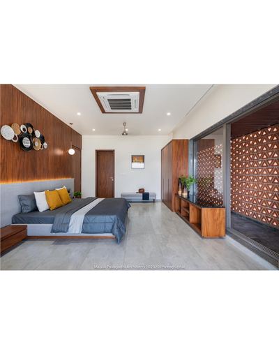 Modern bedroom with wood-panelled headboard wall, floating bed, and perforated jali screen beyond glass doors
