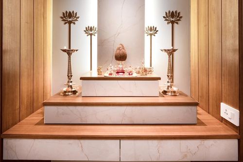 Symmetrical home altar with tiered marble-look platform, brass lotus lamps and backlit wooden niche