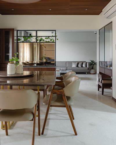 Open dining and living area with wooden chairs, marble table, mirrored partition and greenery