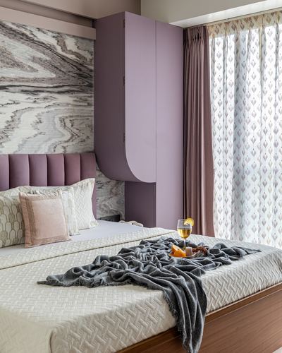 Mauve bedroom with fluted headboard, marble-look wall panel, curved wardrobe and grey throw on bed