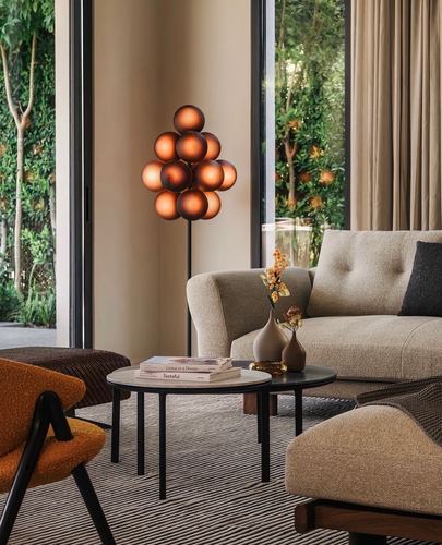 Living room with beige sofa, orange armchair, round coffee tables and a sculptural spherical floor lamp facing garden doors