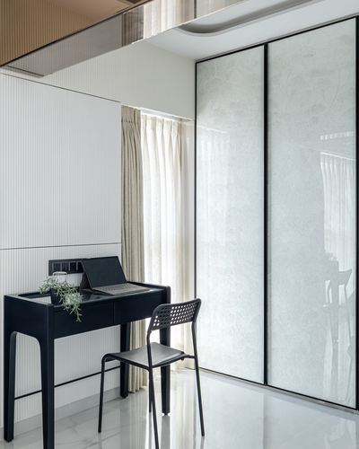 Black study desk with laptop beside sheer curtains and a large textured glass wardrobe wall
