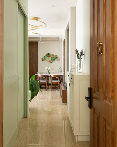 Entry hallway with wooden door and sage cabinetry leading to dining area with circular wall art