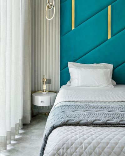 Teal diagonal channel-tufted headboard with gold inlay beside a round white nightstand and sheer curtains