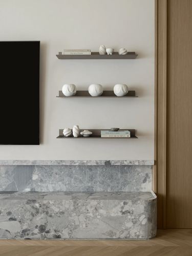 TV wall with floating shelves of ceramic objects above a fluted marble panel and stone bench