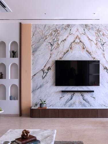 Living room with bookmatched marble TV wall, fluted wood strip, and arched niche display shelf