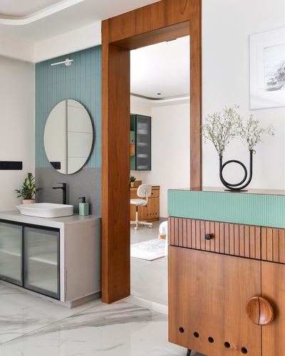 Bathroom with teal tile and round mirror seen through a chunky wood door frame beside a study