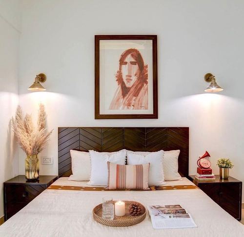 Bedroom with chevron wood headboard, framed portrait sketch, brass sconces, and pampas grass arrangement