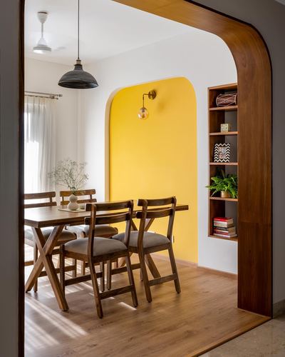 Dining nook with wooden table and chairs framed by a curved mustard archway and wooden shelving