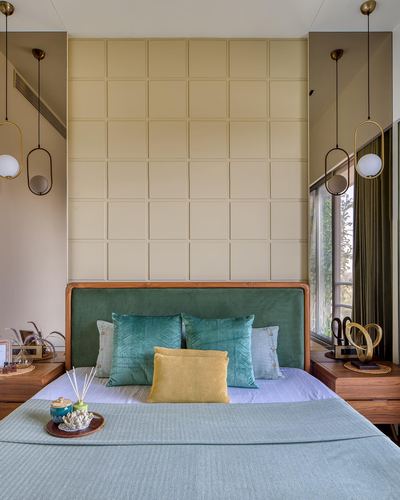 Bedroom with green upholstered headboard, grid-paneled wall, and brass pendant lights on either side.