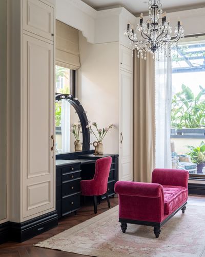 Cream dressing nook with black arched bulb mirror, pink velvet chair and chaise, crystal chandelier