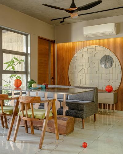 Dining nook with glass table, wooden chairs, grey banquette, and circular carved mirror panel on wood wall