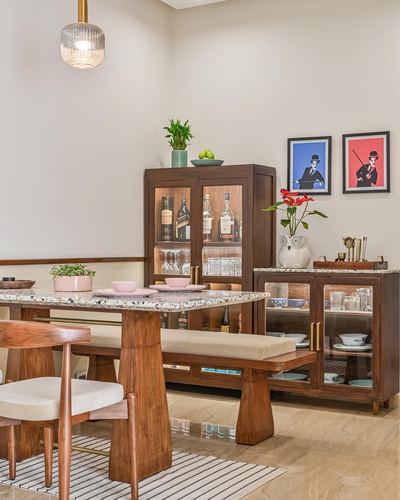 Wooden dining table with terrazzo top, bench, and wooden bar cabinets against beige wall