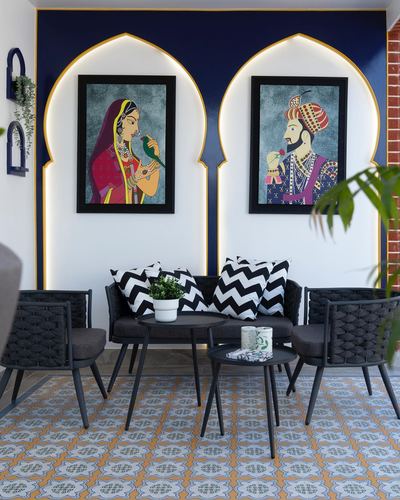 Balcony seating nook with two backlit arches, framed Indian portrait art, black rope chairs, chevron cushions, patterned floor tiles