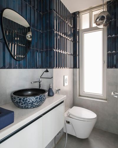 Compact bathroom with ribbed navy tile wall, oval mirror, patterned vessel sink and wall-hung toilet