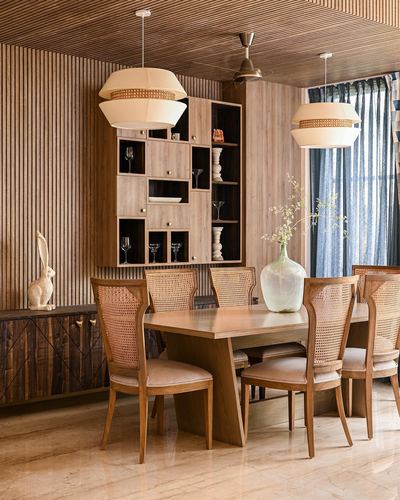 Dining room with fluted wood walls, cane pendant lights, cane-back chairs and a wooden display cabinet
