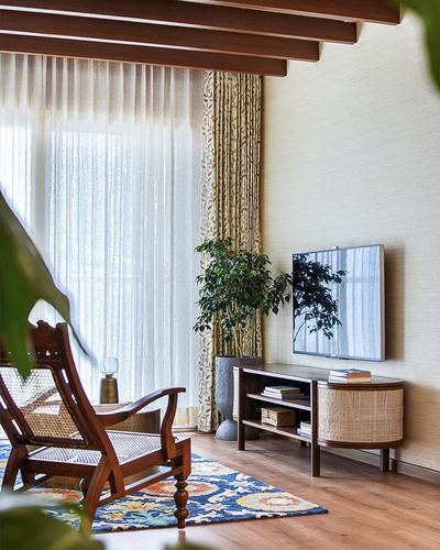 Living room corner with cane armchair, wood tv console, sheer curtains and exposed beams