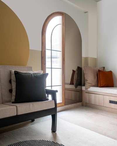 Living room corner with arched wooden window, mustard mural, bench and window seat with cushions