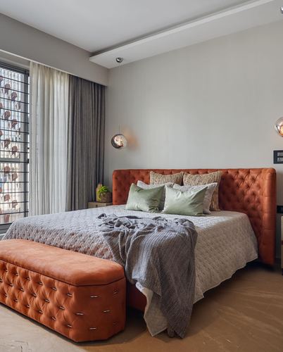 Bedroom with tufted orange leather headboard, grey bedding, sage cushions, and pendant lights