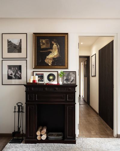 Dark wood fireplace mantel with gallery wall above, opening to a wood-floored hallway beyond