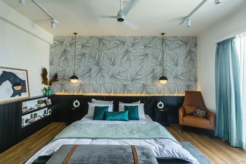 Bedroom with teal bedding, leaf-print wallpaper, hanging pendant lights and tan leather armchair