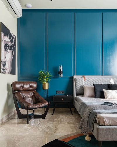 Bedroom with teal paneled wall, brown leather lounge chair, and grey quilted headboard on marble floor