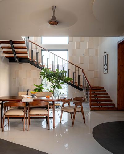Open dining area beneath a floating wooden staircase with textured wall and indoor plant