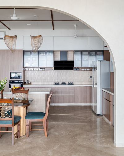 Kitchen seen through arched opening with ribbed cabinetry, woven pendant lights, and marble flooring