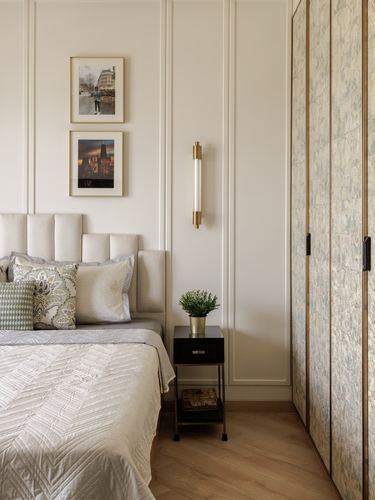 Cream paneled bedroom with upholstered headboard, brass sconce, and patterned wardrobe door