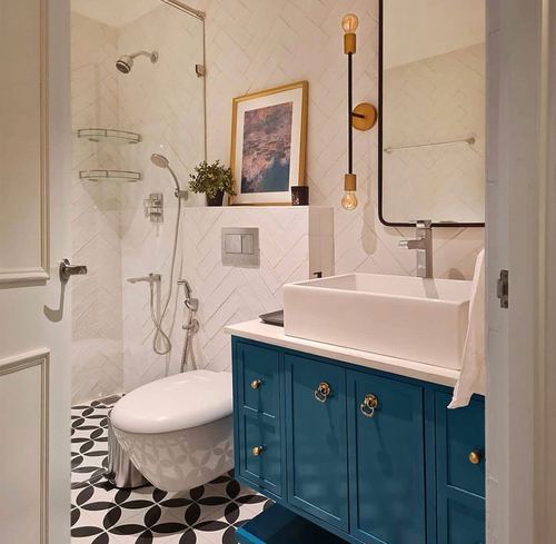 Bathroom with herringbone tile, teal vanity with brass handles, patterned black and white floor