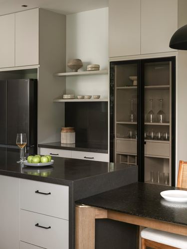 Minimalist kitchen with black stone island, glass cabinet display and ceramic vessels on floating shelf
