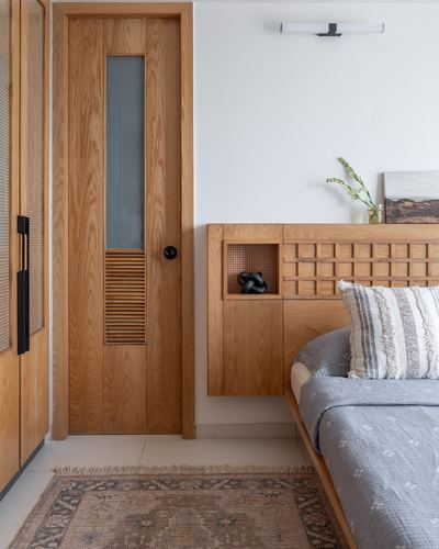Wooden bedroom door beside a floating headboard with cane niche and grey bedding