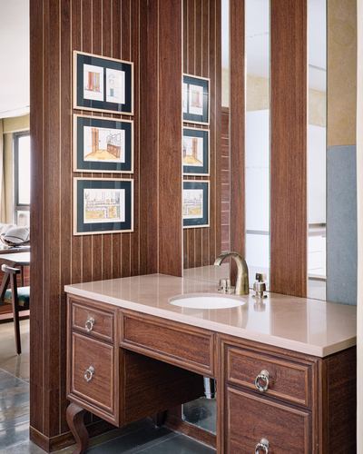 Wood-panelled bathroom vanity with marble-look countertop, brass faucet, and framed sketches above