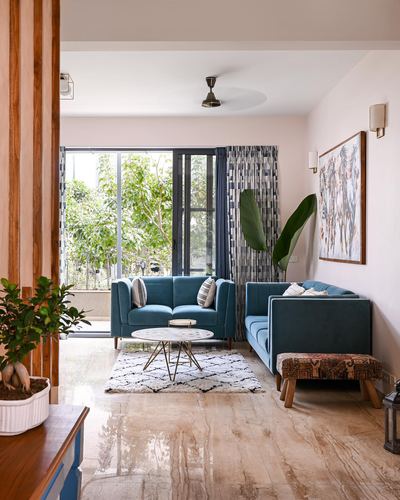 Living room with teal sofas, round coffee table, patterned rug, and glass door opening to greenery.