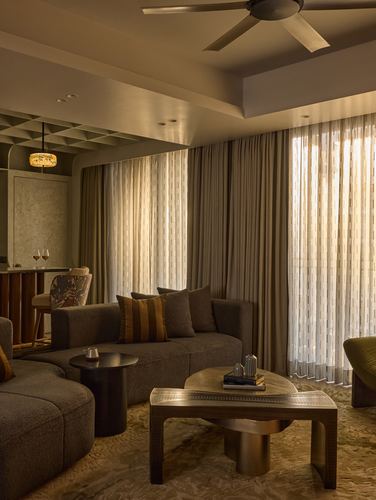 Warm-lit living room with curved sofa, sculptural coffee table, and sheer curtained windows