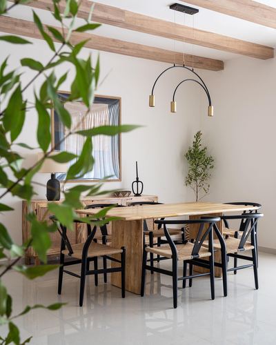 Wooden dining table with black wishbone chairs under an arc pendant light, wood-beamed ceiling