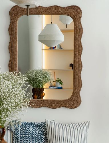 Scalloped rattan mirror reflecting a fabric pendant light and shelving above striped cushions