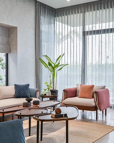 Living room with curved sofa, rust armchair, nested wood coffee tables and sheer curtains