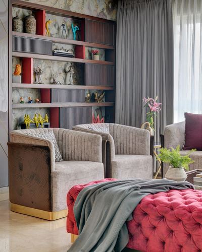 Living room with fluted bookshelf, velvet armchairs, and a red tufted ottoman with throws