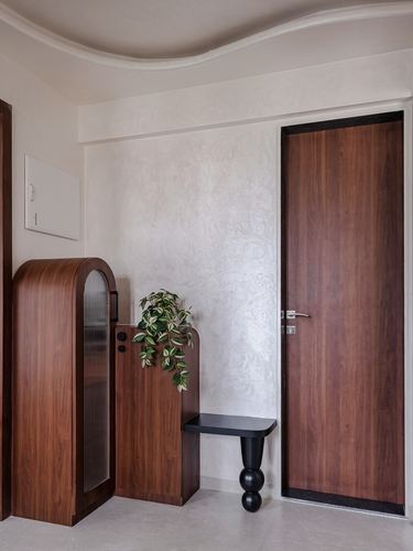 Entryway with arched wood cabinet, textured plaster wall, black bench, and wooden door.