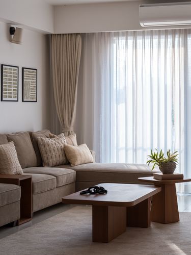 Beige sectional sofa with wooden coffee tables beside sheer curtained window in a minimalist living room
