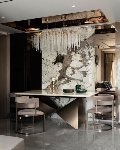 Dining area with bookmatched marble wall, sculptural gold table base, and crystal chandelier
