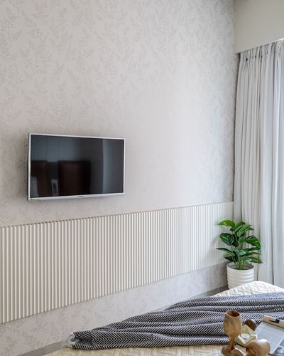 bedroom wall with textured wallpaper, mounted tv, fluted wainscoting, and a plant beside curtained window