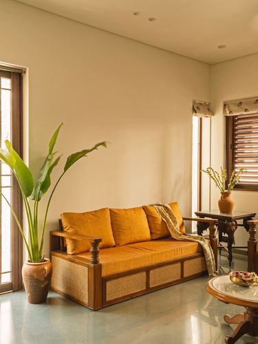 Living room corner with cane sofa, mustard cushions, terracotta planter and terrazzo floor in soft daylight