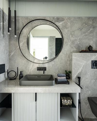 Grey stone bathroom vanity with round black mirror, rectangular sink, and fluted wood cabinet doors