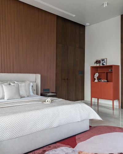 Bedroom with fluted terracotta wood headboard wall, dark wardrobe, and orange cabinet accent