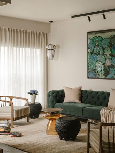 Living room with green tufted sofa, carved black stools, and botanical wall art